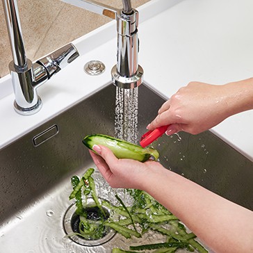Cropped view of female hands peeling cucumber over Food waste disposer machine in sink in modern kitchen
